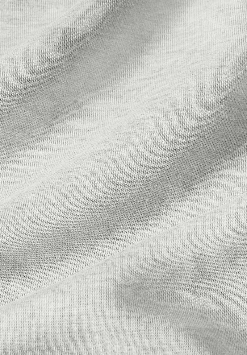 Nahaufnahme eines weichen, hellgrauen Stoffes, der eine feine Strickstruktur mit sanften Falten und subtilen Schatten zeigt.