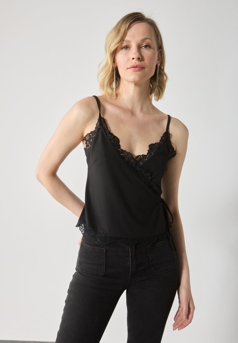 Svart satinkjole med blonderdetaljer langs halsen og kanten, med tynne stropper og en omslagskonstruksjon. Kombinert med svarte jeans.