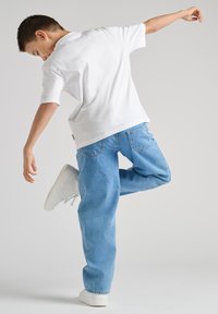Camiseta blanca de algodón combinada con jeans de denim azul. Los jeans tienen un ajuste relajado y están remangados en los puños, complementados con zapatillas blancas.