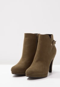 Bottines en daim vert olive avec un bout effilé, un talon haut, une fermeture éclair latérale et un accent de boucle décorative sur le côté extérieur.