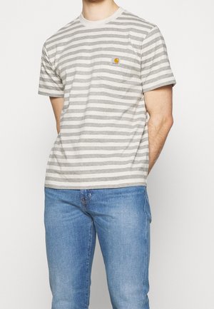 Homme portant un T-shirt à manches courtes rayé gris et blanc avec une poche poitrine et un jean en denim bleu sur fond blanc.
