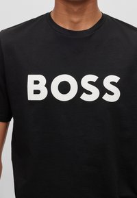 Schwarzes Baumwoll-T-Shirt mit Rundhalsausschnitt, auf der Vorderseite zentriert mit auffälligem weißen "BOSS"-Text. Kurze Ärmel, glatte Textur.