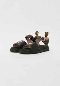 Sorte sandaler med åpen design, med hjerteutskjæring, justerbar stroppe og gule trekkstropper. Teksturert såle og sømdetaljer.