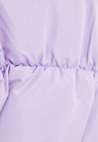 Jasnofioletowa, gładka tkanina z marszczeniem w talii, tworząca miękki, teksturowany wygląd. Materiał wydaje się lekki i błyszczący.