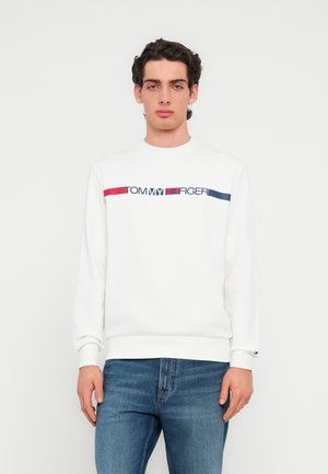 Λευκό φούτερ με στρογγυλή λαιμόκοψη και ριμπ μανσέτες, με πολύχρωμη ρίγα λογότυπου "TOMMY HILFIGER" στο στήθος. Συνδυασμένο με μπλε τζιν.