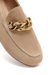 Beige Wildleder Slipper mit runder Zehenform und einer goldfarbenen Kettenakzent am Spann. Mit Stich entlang der Kante. Glatte Innenauskleidung.