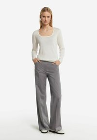 Vit långärmad topp med fyrkantig halsringning, kombinerad med grå vida byxor. Outfiten har mjuka texturer och subtila linjer.