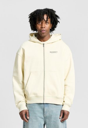 Light yellow zip-up hoodie made of soft material, featuring a front pocket and "RETERNITY" text on the left chest. Casual fit with a hood.