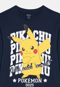 Mornarska majica s Pikachu likom koji preklapa ruke, tekst "Pikachu" ponovljen, "Moramo ih sve uhvatiti!!" i "Pokémon 0025" na dnu.