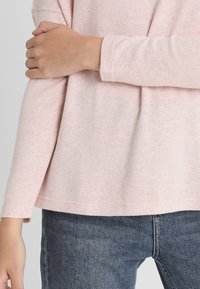 Långärmad tröja i mjuk rosa bomullsblandning, med en avslappnad passform och subtil textur. Sömslutet slutar precis nedanför midjan.