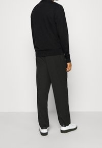 Svart stickad tröja med rund halsringning, kombinerad med löst sittande svarta byxor och vita sneakers med svarta detaljer.