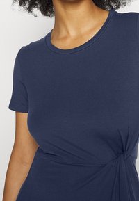 Granatowa sukienka w T-shircie wykonana z miękkiej bawełny, z okrągłym dekoltem i skręconym węzłem w pasie dla dodatkowego zdobienia.