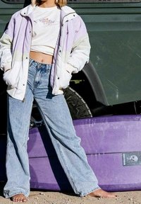 Kleurige jas in lavendel en wit, gecombineerd met lichtblauwe jeans met wijde pijpen; paarse surfplank op de achtergrond met een schedelafbeelding.