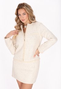 Cremfarbener, strukturierten Blazer mit passendem Rock, der ein kragenloses Design, lange Ärmel und subtile metallische Fäden aufweist.