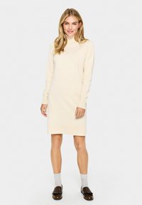 Bežs adīts kleita ar augstu apkakli, garām piedurknēm, ribotām aprocēm un maliņu. Vienkāršs, taisns dizains ar maigu tekstūru.