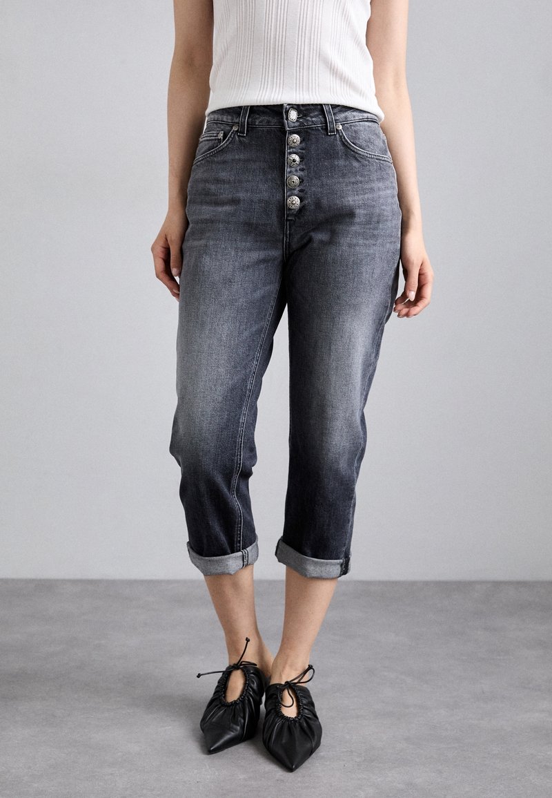 Napapadi, keskmise tõusuga tumehallid denim teksad, mis on rullitud äärtega ja laia lõikega, koos mustade volditud kannaga kingadega.