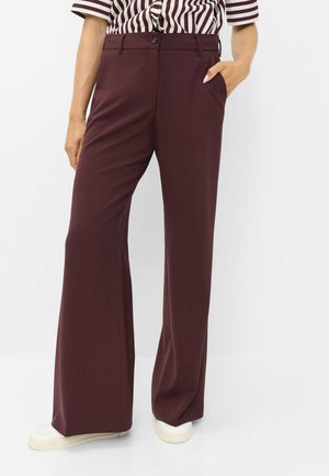 Woman wearing high-waisted wide-leg dark purple trousers, striped shirt tucked in, white sneakers, with one hand in pocket.