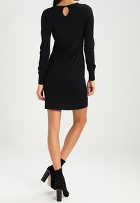 Robe noire à manches longues avec un dos en trou de serrure, silhouette ajustée et tissu doux. Associée à des bottines noires à talons.