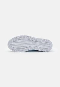 Semelle de chaussure blanche avec un motif ondulé texturé et un logo Puma centré sur la semelle extérieure en caoutchouc sur un fond uni.