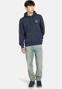 Felpa blu navy in cotone, con tasca frontale e logo sul petto. Abbinata a jeans azzurri e scarpe blu navy.