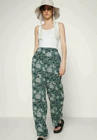 Calças verdes com padrão floral, feitas de tecido leve, com pernas largas e uma cintura alta, combinadas com uma t-shirt branca e sandálias.