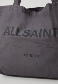 Borsa tote in tessuto grigio scuro con testo nero che recita "ALLSAINT" in corsivo, e "LONDON" sottostante.