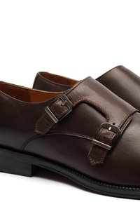 Hnědé kožené boty s hladkým povrchem, ozdobené dvěma stříbrnými sponami a kontrastním šitím. Nízký podpatek a zaoblený špičkový design.