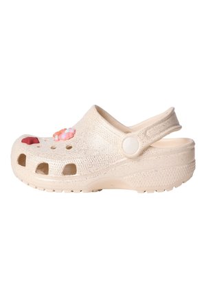 Beiger Schaumsclog mit Riemen hinten und Belüftungslöchern, verziert mit pink-, rot- und weißfarbenen blumenförmigen Anhängern am oberen Bereich.