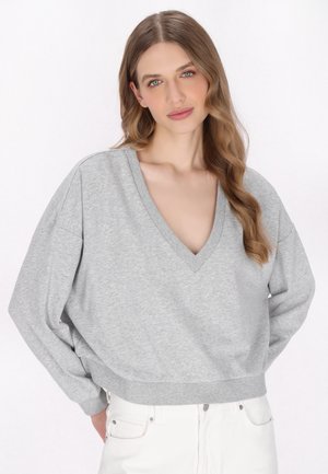 Grå sweatshirt med V-hals, løs pasform og ribbet kant. Blødt stof med dropped shoulders, båret med hvide jeans.