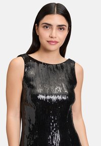 Czarna sukienka z cekinami o okrągłym dekolcie i bezrękawowym kroju. Cekiny tworzą błyszczącą, teksturowaną powierzchnię, która łapie światło.