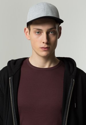 Cappellino da baseball grigio con visiera nera, indossato da una persona con una felpa nera con zip sopra una maglietta bordeaux. Design minimalista con texture lisce.
