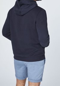 Mörkblå hoodie med slätt tyg och ribbade muddar, tillsammans med ljusblå uppvikt shorts. Bakvy, minimal design.