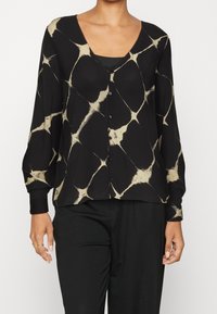 Cardigan nero con un motivo irregolare color crema, dotato di scollo a V, chiusura con bottoni e maniche lunghe con polsini aderenti.