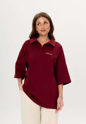 Bordeaux oversized polo-shirt met een kraag, korte mouwen, een losse pasvorm en een klein logo in gouden borduring op de borst. Zacht katoenmateriaal.
