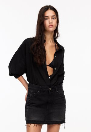 Czarna, oversize koszula z guzikami i podwiniętymi rękawami, noszona na czarnym bikini. W połączeniu z czarną denimową mini spódnicą z postrzępionym dołem.