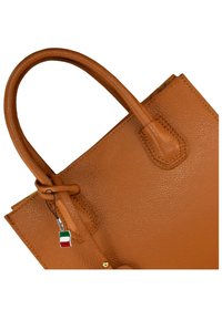Tan leren handtas met een textuur, twee stevige handvatten en een decoratief label met de Italiaanse vlag. Rectangulaire vorm, zonder zichtbare sluiting.