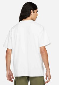 White cotton T-shirt with short sleeves, relaxed fit, no visible patterns or accents, viewed from the back. Paired with olive green shorts.