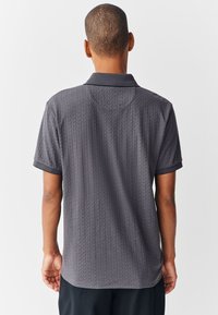 Donkergrijs poloshirt met een gestructureerd visgraatpatroon, kraag en korte mouwen. Afgewerkt met een effen zwarte bies aan de kraag en mouwen.