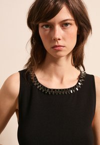 Abito nero senza maniche con scollo rotondo decorato con dettagli in perline di cristallo. Texture liscia, design aderente.