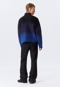 Pull colletto alto in nero e blu, morbido e sfumato, con vestibilità rilassata, abbinato a pantaloni neri con righe sottili.