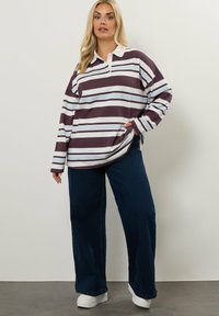 Överdimensionerad randig pikétröja med mörk vinröda och ljusblå ränder, med krage och långa ärmar, i kombination med vida mörk denimbyxor.