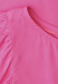 Gros plan d'un vêtement rose montrant un détail de tissu froncé sur la manche et une encolure cousue avec une bordure étroite en tissu.