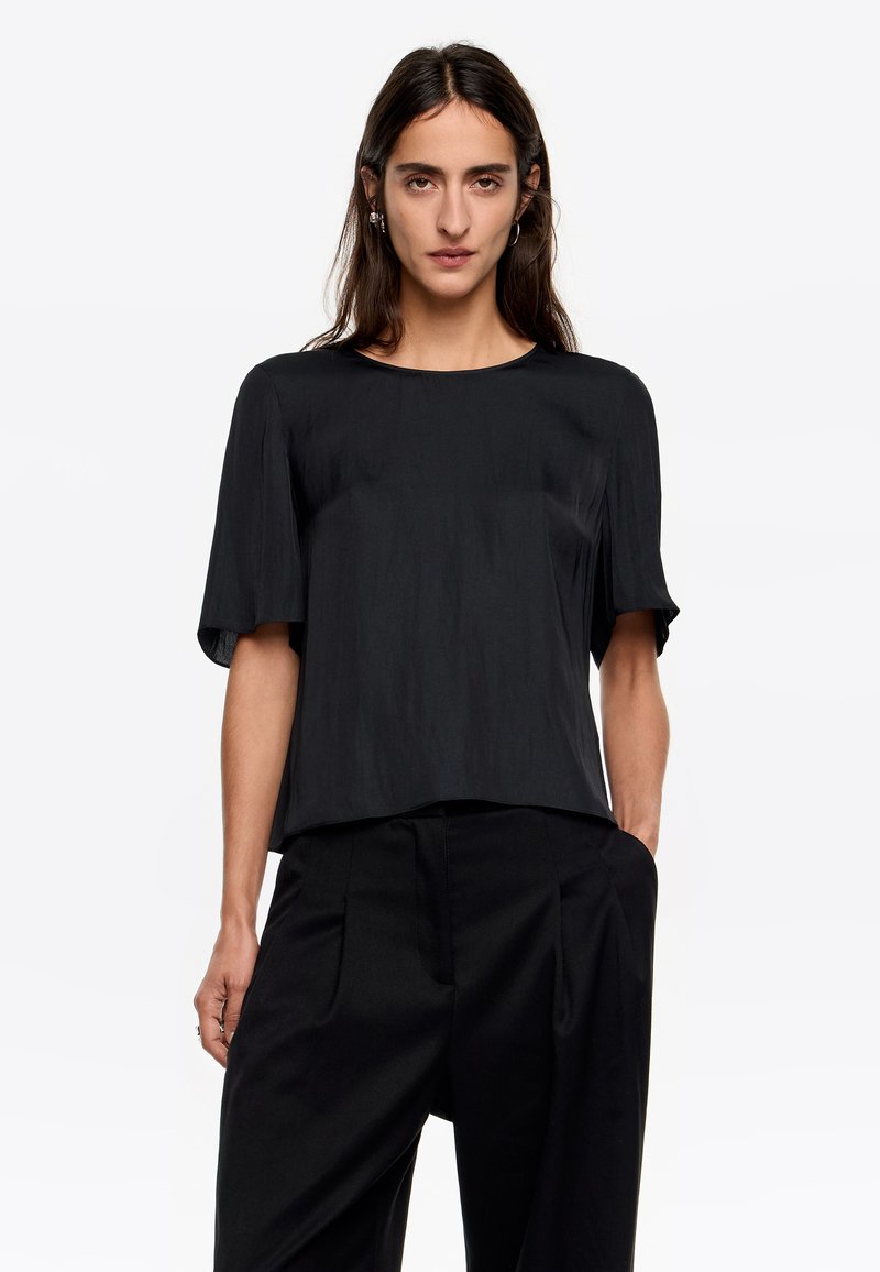 Czarny krótki top z krótkim rękawem wykonany z gładkiego, lekkiego materiału; posiada okrągły dekolt i luźny krój, zestawiony z dopasowanymi czarnymi spodniami.