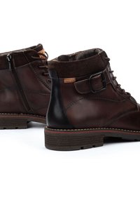 Botas de tobillo de cuero marrón con un collarín de ante, cremallera lateral, parte delantera con cordones y un acento de cuero negro en el talón. Suela de madera resistente.