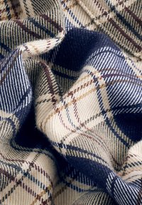 Tissu doux avec un motif à carreaux beige, marine et marron, montrant des plis et la texture du matériau tissé.