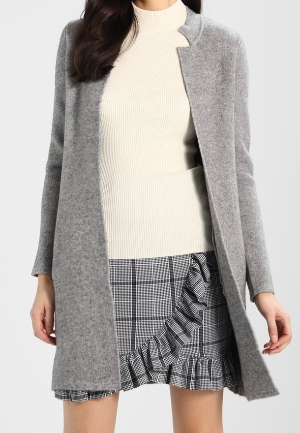 Szary płaszcz z mieszanki wełny o prostym kroju i otwartym przodzie, zestawiony z kremowym swetrem w prążki oraz czarno-białą, kratkowaną spódnicą z falbankami.