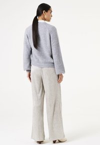 Grijze wollen trui met een gestructureerde afwerking, gecombineerd met glanzende zilveren broek met brede pijpen. De ensemble heeft een gestroomlijnde silhouet en lange mouwen.