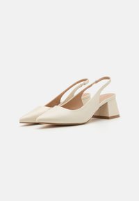 Beige színű, hegyes orrú, slingback sarkú cipők sima bőrből, stabil, szögletes blokk sarkukkal. Minimalista forma jellemzi őket.