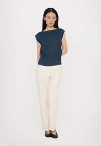 Marineblauw geribbelde mouwloze top met een bootnek, gecombineerd met crèmekleurige rechtgesneden broek en zwarte ballerina's. Eenvoudig, strak ontwerp en neutrale kleuren.