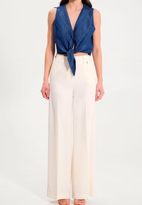 Pantalon écru à jambes larges et taille haute, associé à un haut court bleu sans manches avec un nœud sur le devant en tissu denim.